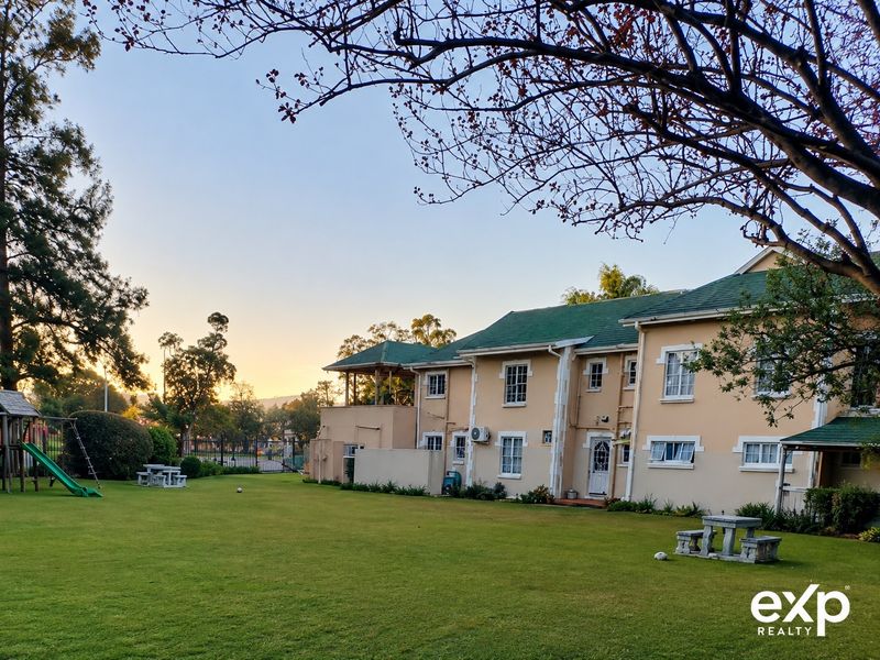 A view of the rear exterior of the apartment complex, featuring a well-maintained lawn, green tiled roof, and established garden surroundings.