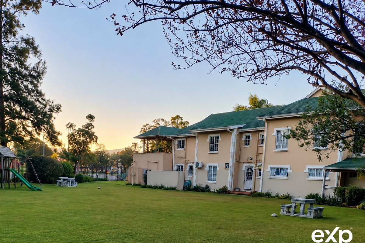 A view of the rear exterior of the apartment complex, featuring a well-maintained lawn, green tiled roof, and established garden surroundings.