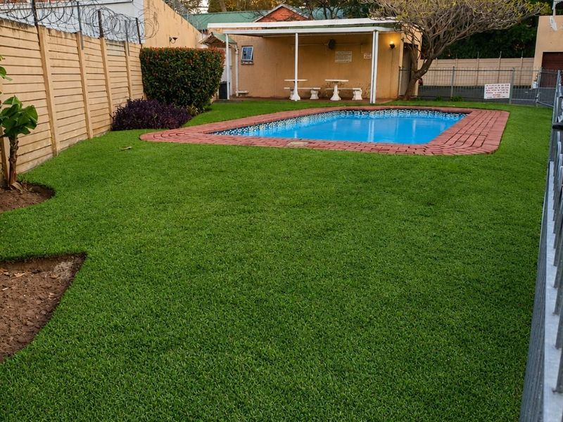 A well-maintained backyard featuring a swimming pool with brick coping, a covered patio area, and a manicured lawn enclosed by perimeter fencing.