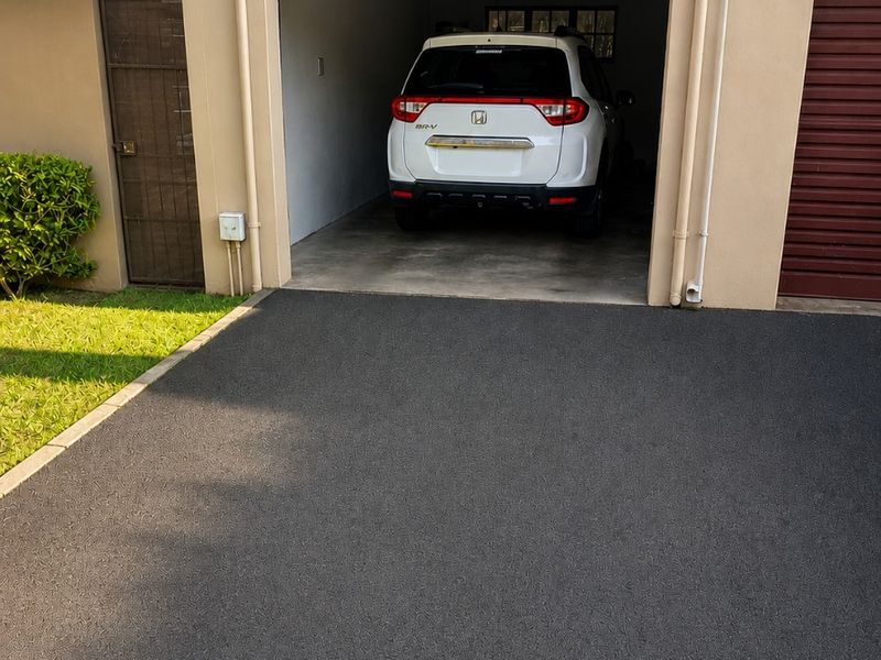 A paved driveway leading to a single garage unit with exterior fire safety signage and a side pedestrian gate.