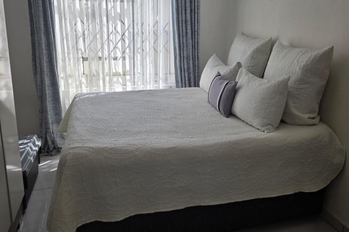 A bedroom featuring tiled flooring and a built-in wardrobe, with natural light entering through a window dressed with curtains.