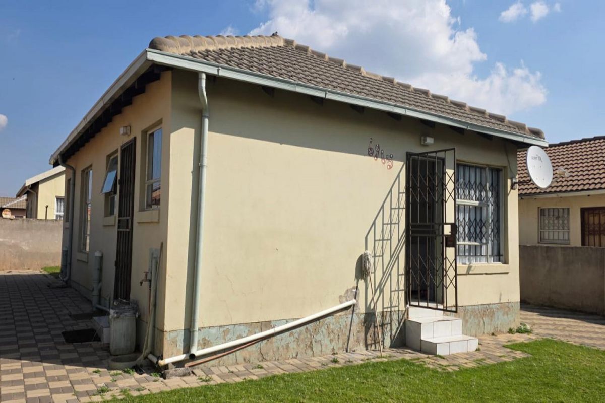 Exterior view of a detached house featuring a tiled roof, security gates, and paved surroundings with visible wear to the exterior wall finishes.