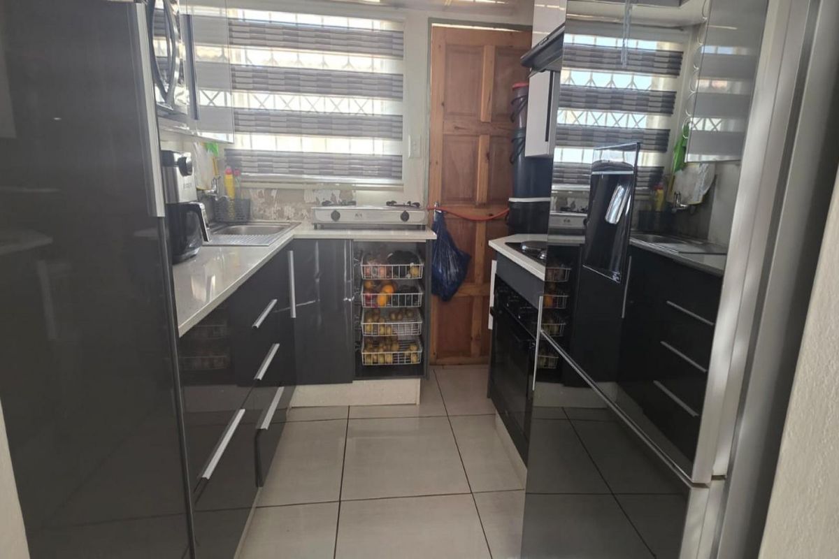Compact kitchen featuring modern high-gloss cabinetry, stone-look countertops, tiled flooring, and a built-in oven and hob.