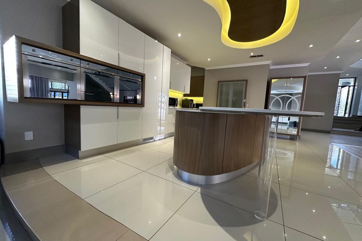 Modern kitchen featuring high-gloss cabinetry, a central island with integrated appliances, and a distinctive illuminated ceiling bulkhead with polished tile flooring.