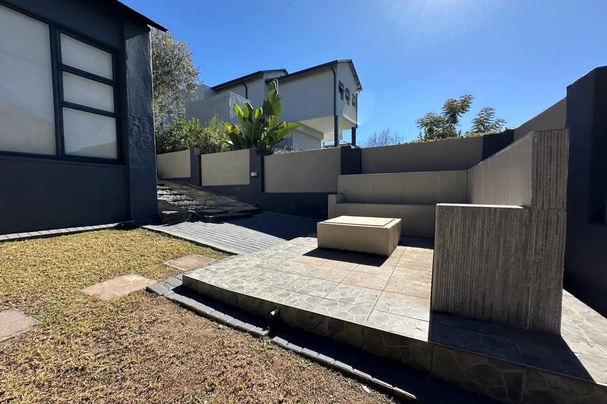 A private rear garden area featuring a raised tiled patio with built-in concrete seating, paved pathways, and secure boundary walls.
