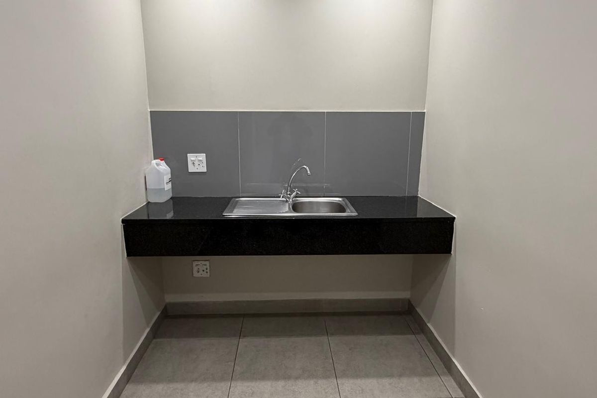 A compact office kitchenette area featuring a black granite countertop, stainless steel sink, and grey tiled splashback.