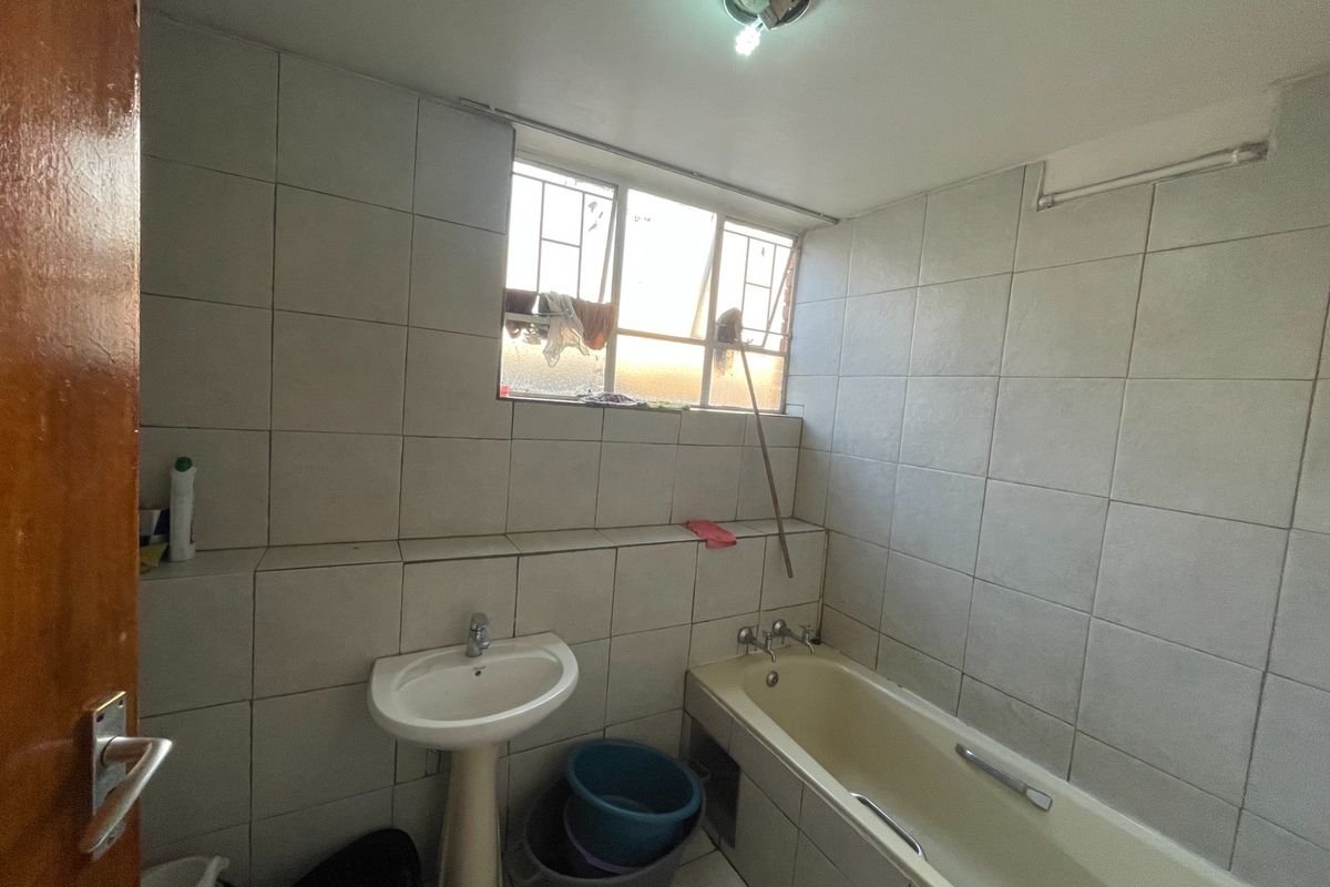 A dated bathroom featuring full-height wall tiling, a pedestal basin, and a built-in bathtub with a window for natural light.