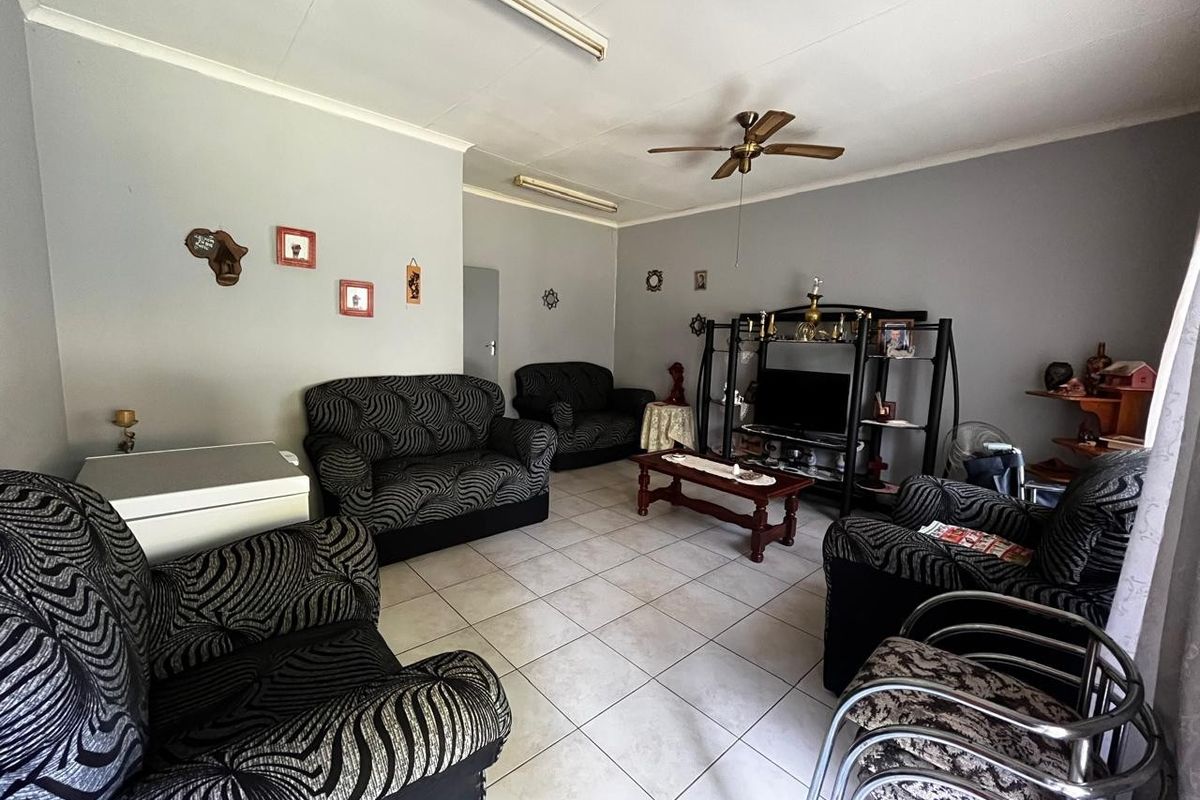 A spacious living room featuring neutral wall tones, tiled flooring, and a ceiling fan, providing a functional and comfortable family living area.