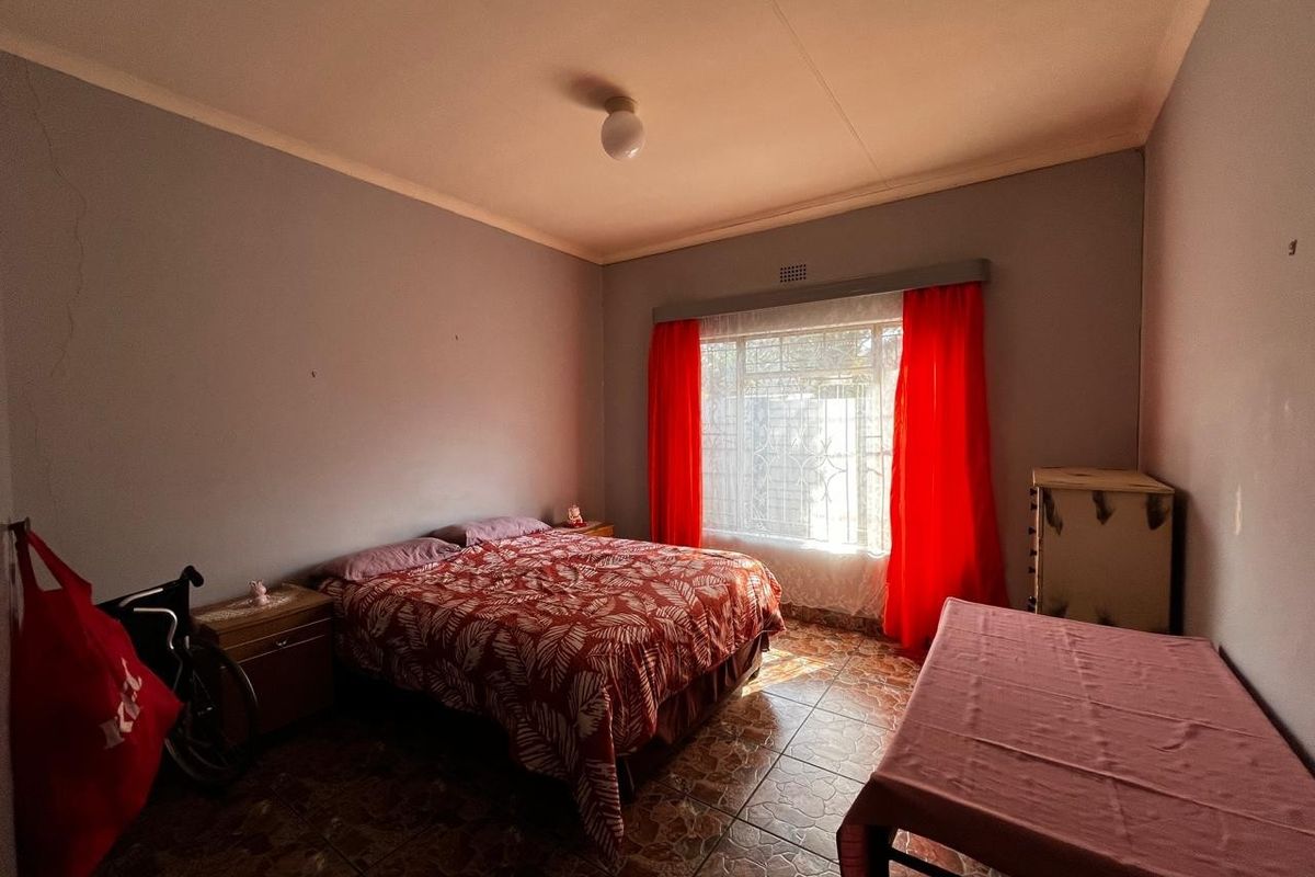 A bedroom featuring tiled flooring, a large window with security bars, and basic wall finishes.