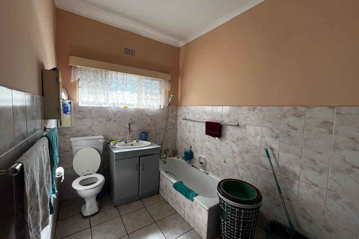 A dated bathroom featuring a built-in bathtub, vanity sink, and toilet with tiled walls and flooring.