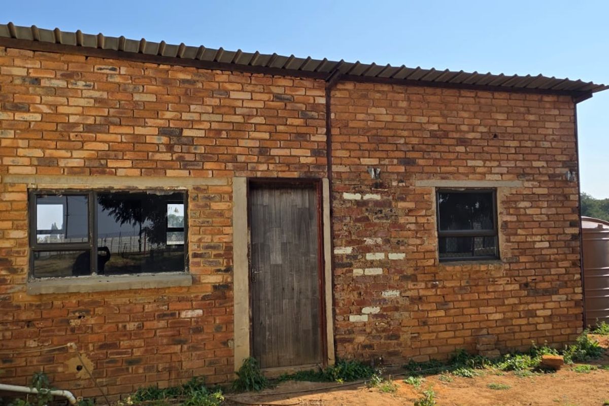 Exterior view of a rustic brick outbuilding featuring a metal roof, timber door, and aluminium-framed windows on a farm property.