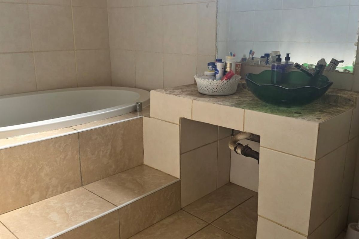 A bathroom featuring a built-in bathtub, tiled vanity area with an integrated basin, and a toilet, requiring cosmetic updates to the vanity and finishes.