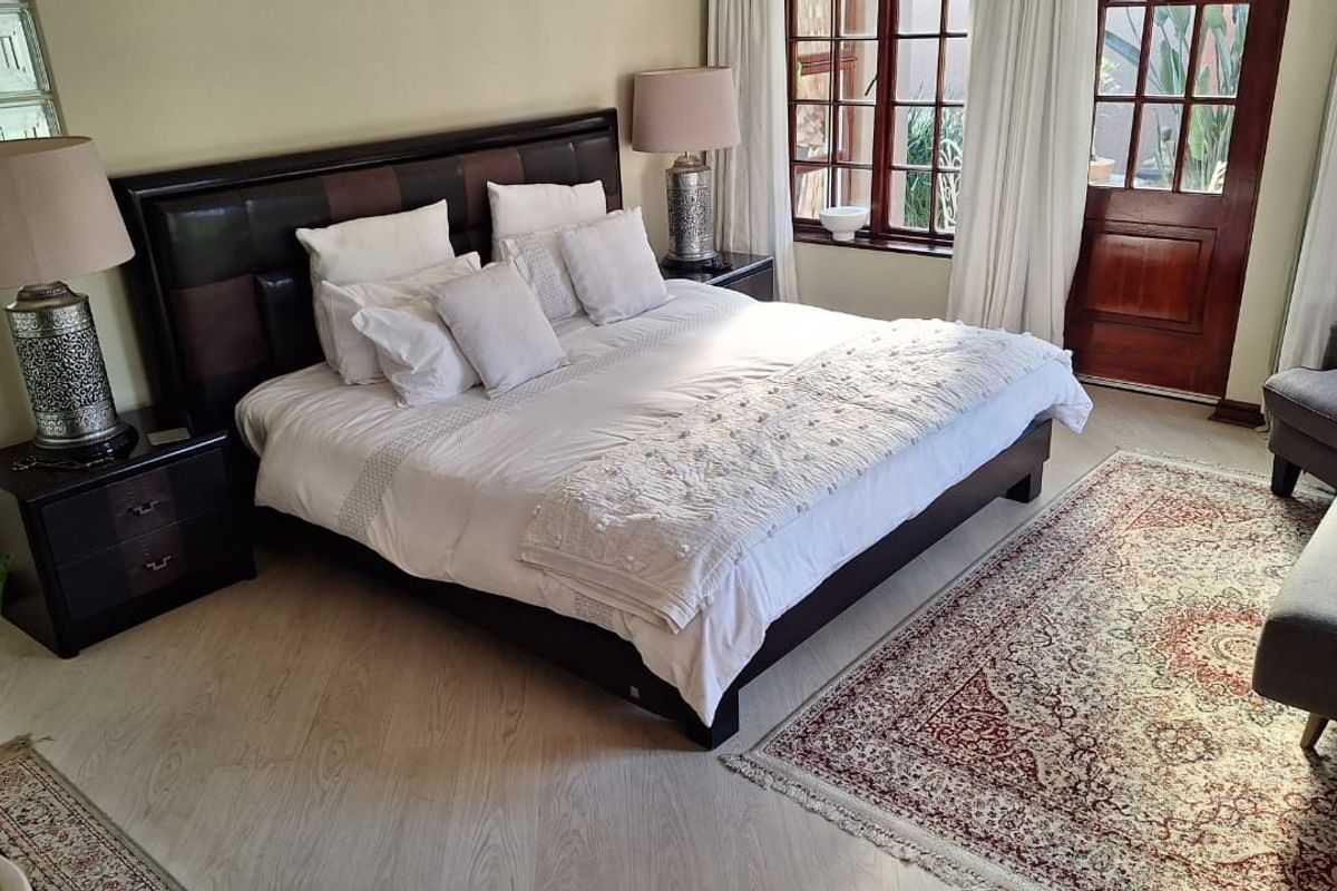 A spacious bedroom featuring light wood-look flooring, large timber-framed windows, and a glass-paneled door providing direct access to the outdoor area.