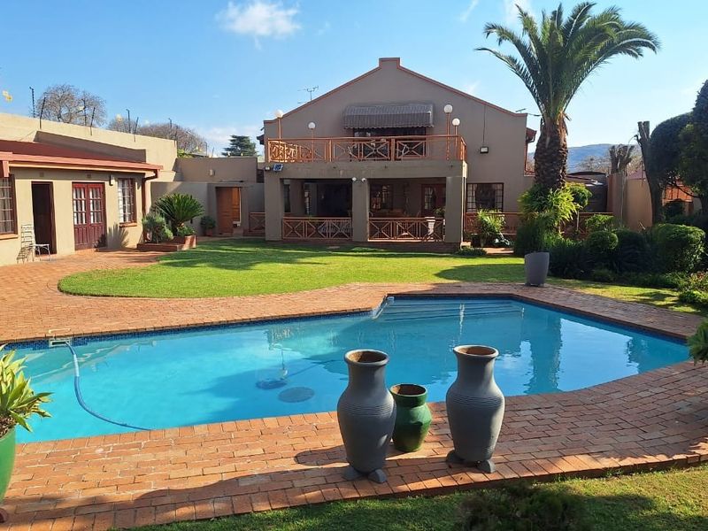 Spacious rear garden featuring a swimming pool, brick-paved patio area, and a multi-level house with a balcony and covered outdoor entertainment space.