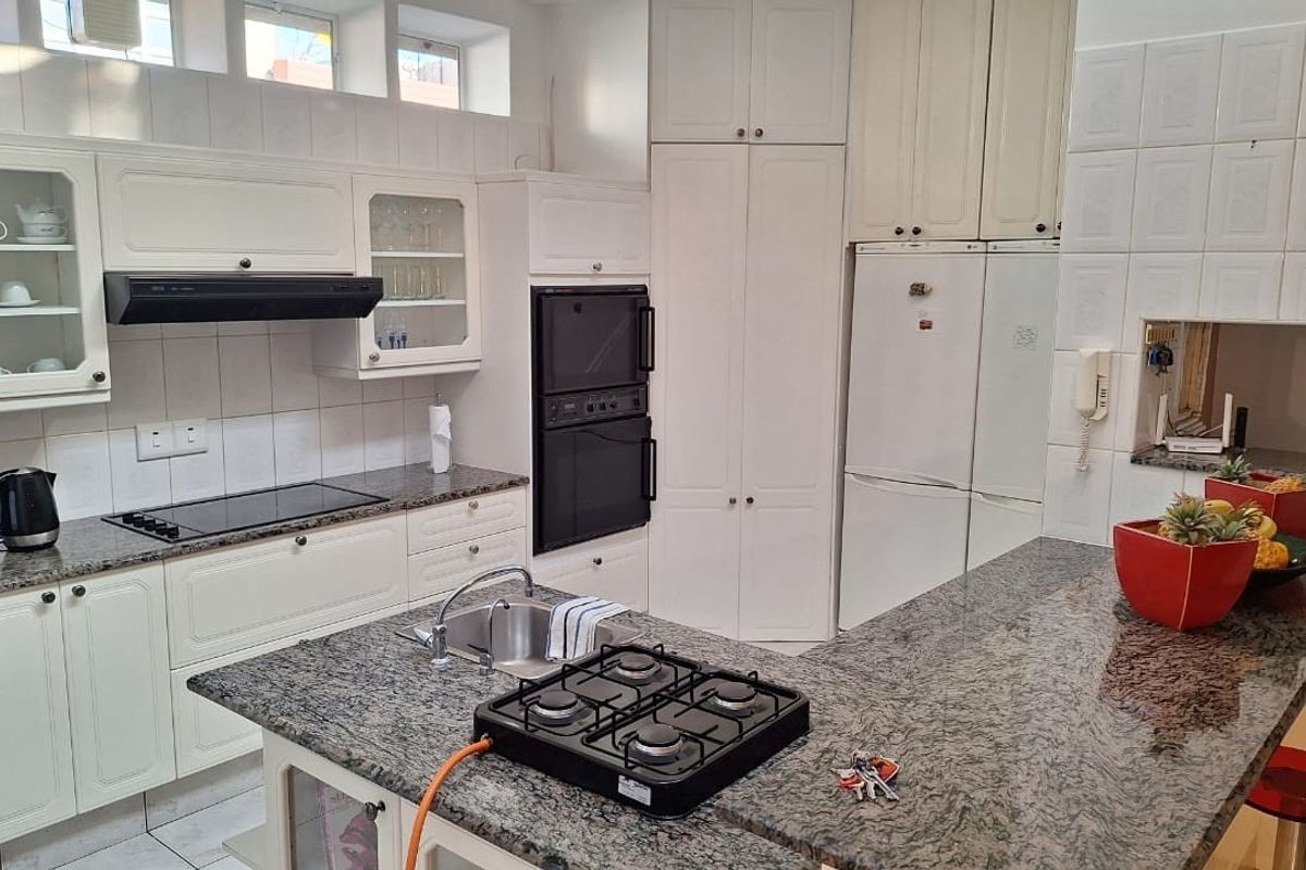 A functional kitchen featuring granite countertops, built-in double ovens, a glass-top stove, and a central island with an integrated gas hob and sink.