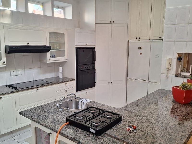 A functional kitchen featuring granite countertops, built-in double ovens, a glass-top stove, and a central island with an integrated gas hob and sink.