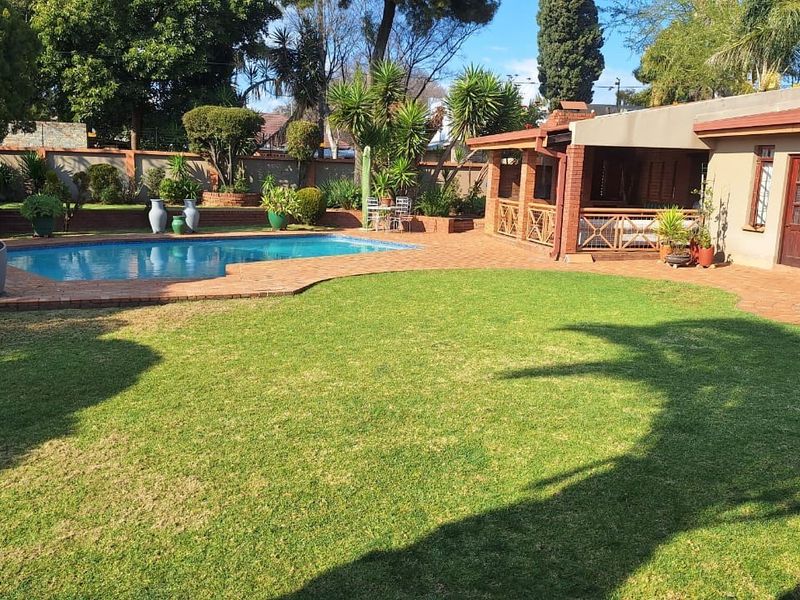 Spacious rear garden featuring a swimming pool, brick-paved patio area, and a covered outdoor entertainment space with brick pillars.
