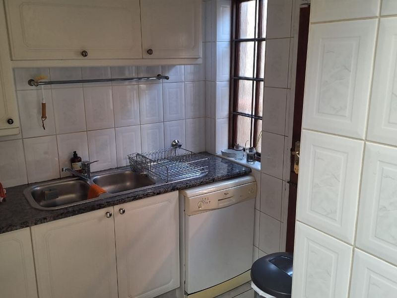 A compact scullery area featuring built-in cabinetry, a double stainless steel sink, tiled splashbacks, and space for an under-counter dishwasher.