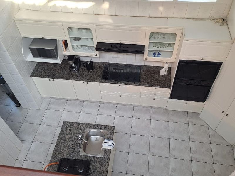 A high-angle view of a functional kitchen featuring granite countertops, built-in oven, hob, extractor fan, and a central island with a prep sink.