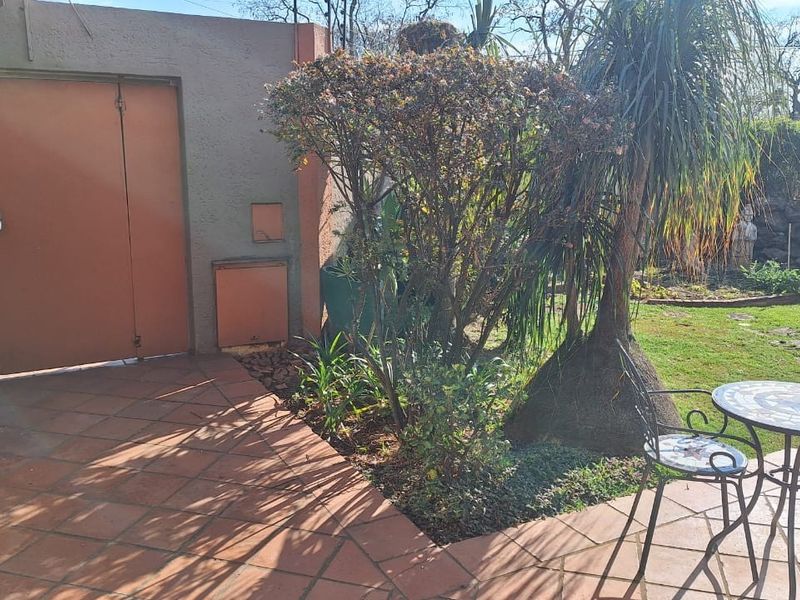 A private rear patio area featuring terracotta tiled flooring, adjacent to a garden space with established trees and shrubs.