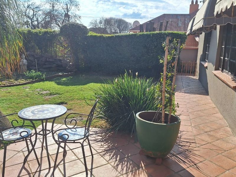 A private rear garden featuring a tiled patio area, established landscaping, and a retractable awning providing shade along the side of the house.