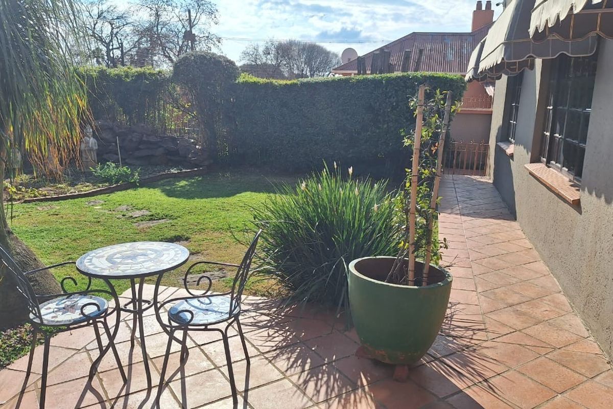 A private rear garden featuring a tiled patio area, established landscaping, and a retractable awning providing shade along the side of the house.