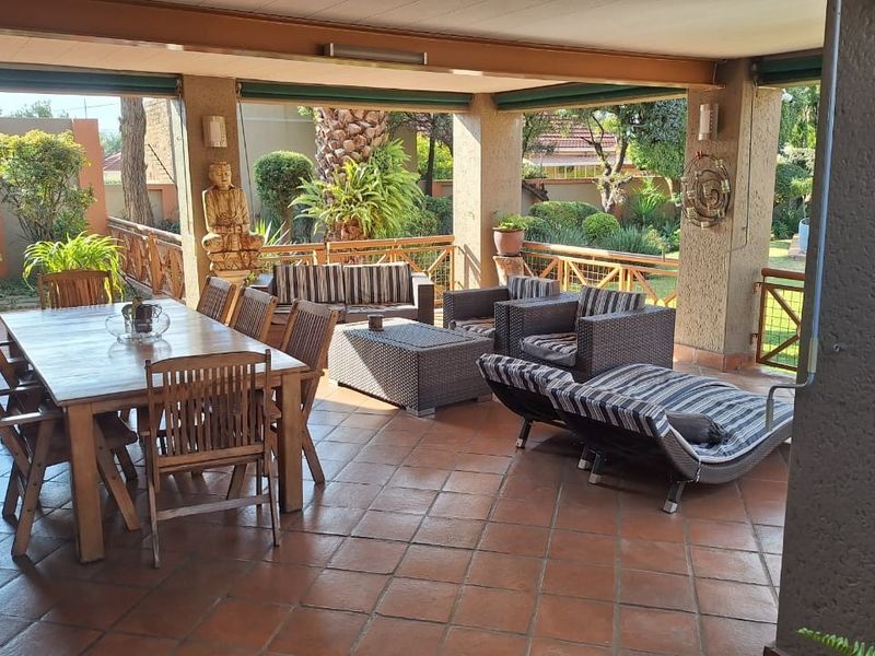 Spacious covered patio featuring terracotta tiled flooring, overlooking a lush garden, ideal for outdoor dining and relaxation.