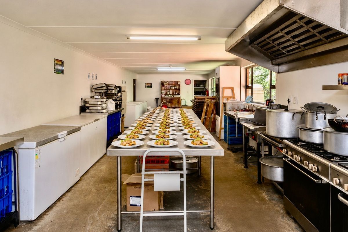 A functional commercial kitchen featuring stainless steel prep surfaces, a large industrial stove with extractor hood, and ample refrigeration space for high-volume food preparation.