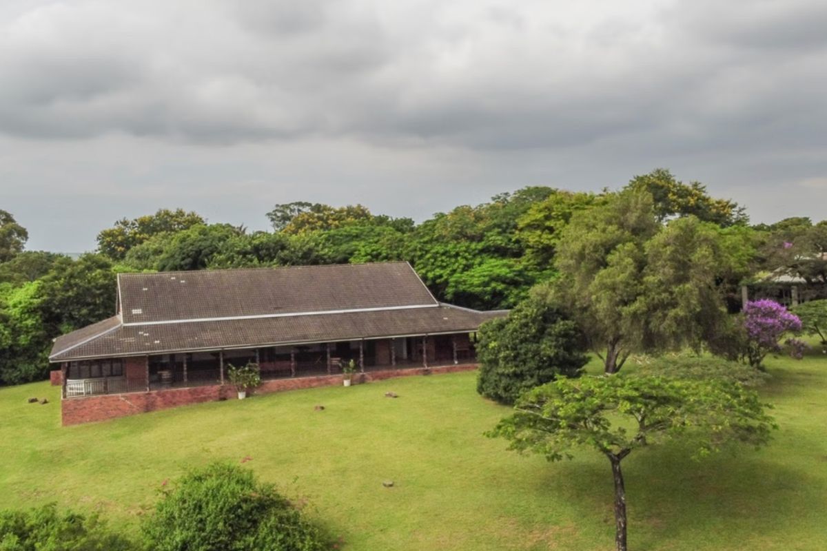 Aerial view of a commercial property featuring a brick building with a tiled roof and a spacious covered veranda set within expansive landscaped grounds.