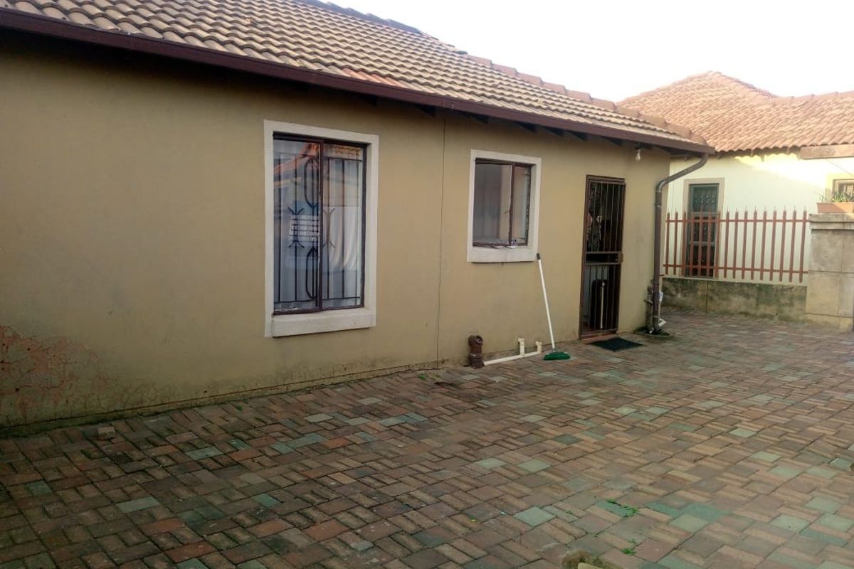 Exterior view of the property featuring a paved courtyard, tiled roof, and security bars on windows and doors.
