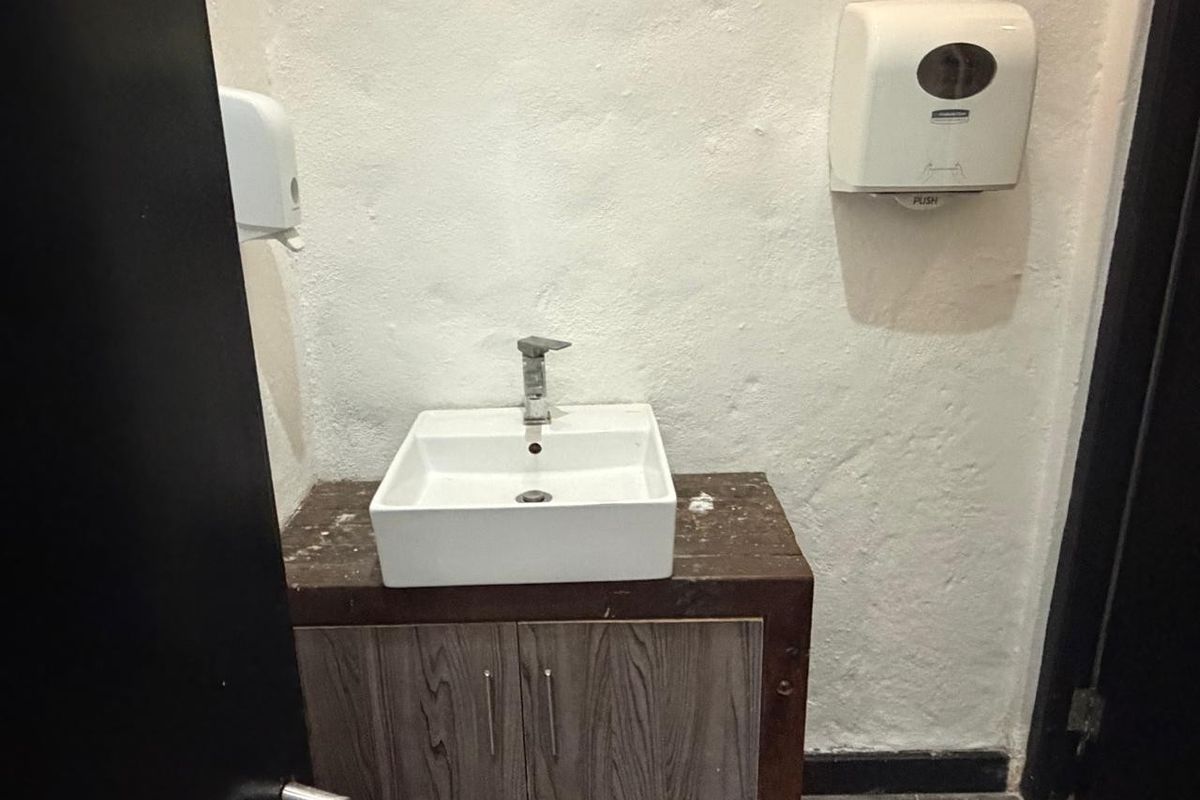 A commercial restroom vanity area featuring a square vessel sink, wood-look cabinetry, and wall-mounted soap and paper towel dispensers.