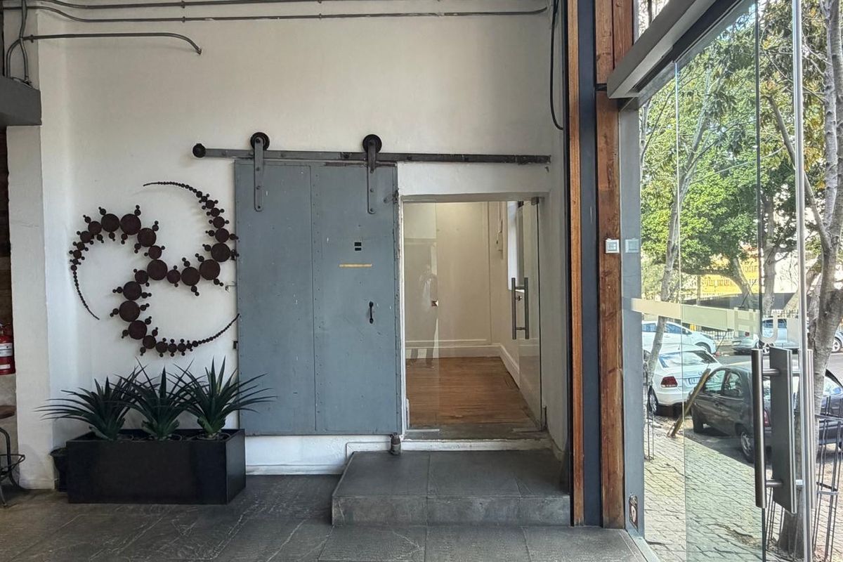 Industrial-style commercial entrance featuring a sliding metal door, exposed conduit, and large glass storefront windows overlooking the street.