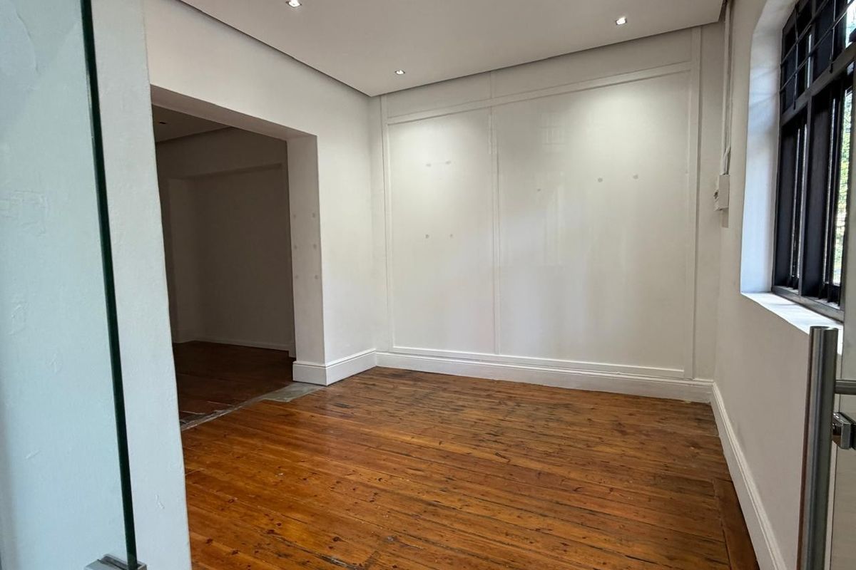 A bright, empty commercial office space featuring polished wooden flooring, recessed ceiling lighting, and large windows allowing for natural light.