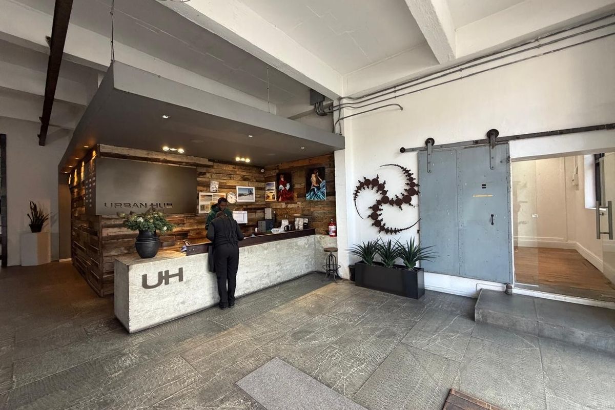 Commercial reception area featuring a concrete service desk, industrial sliding metal door, exposed ceiling beams, and rustic timber wall cladding.