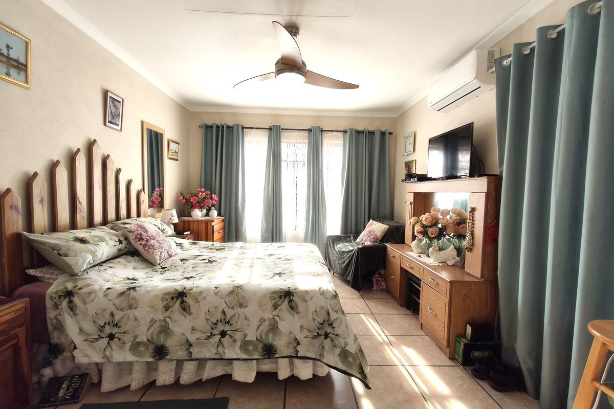 A well-lit bedroom featuring tiled flooring, a ceiling fan, and a wall-mounted air conditioning unit.