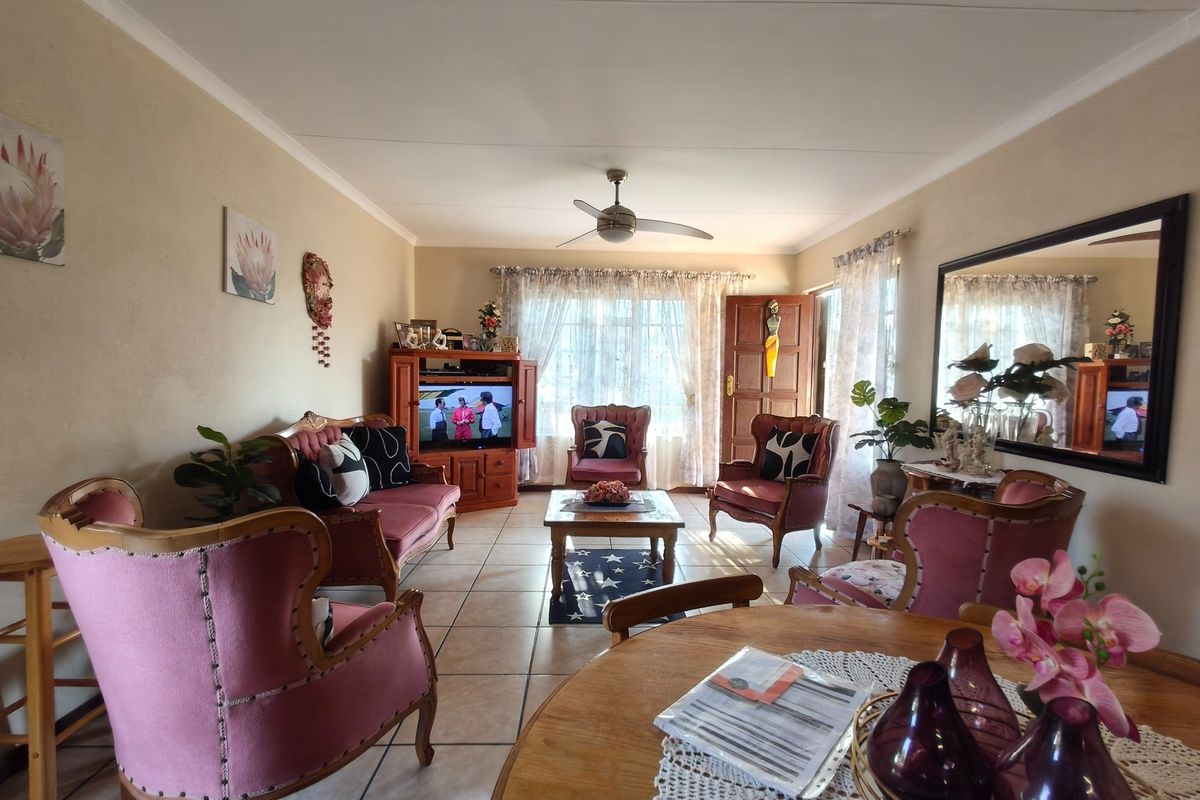 A spacious living room featuring tiled flooring, a ceiling fan, and large windows that provide ample natural light.