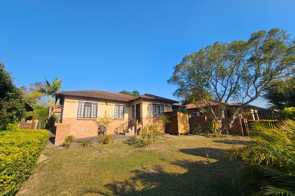 A view of the rear exterior of the house, featuring a brick facade, tiled roof, and a spacious garden area.