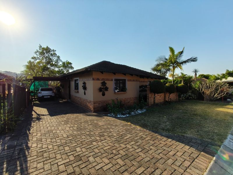 A well-maintained single-story house featuring a paved driveway, covered carport, and established garden with brick boundary walls.