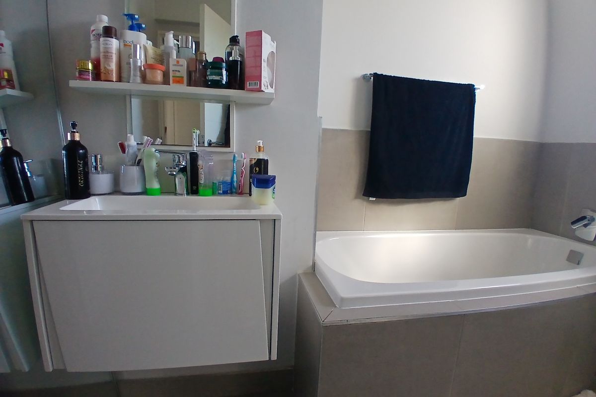 A functional bathroom featuring a wall-mounted vanity with integrated basin, a tiled bathtub surround, and a wall-mounted towel rail.