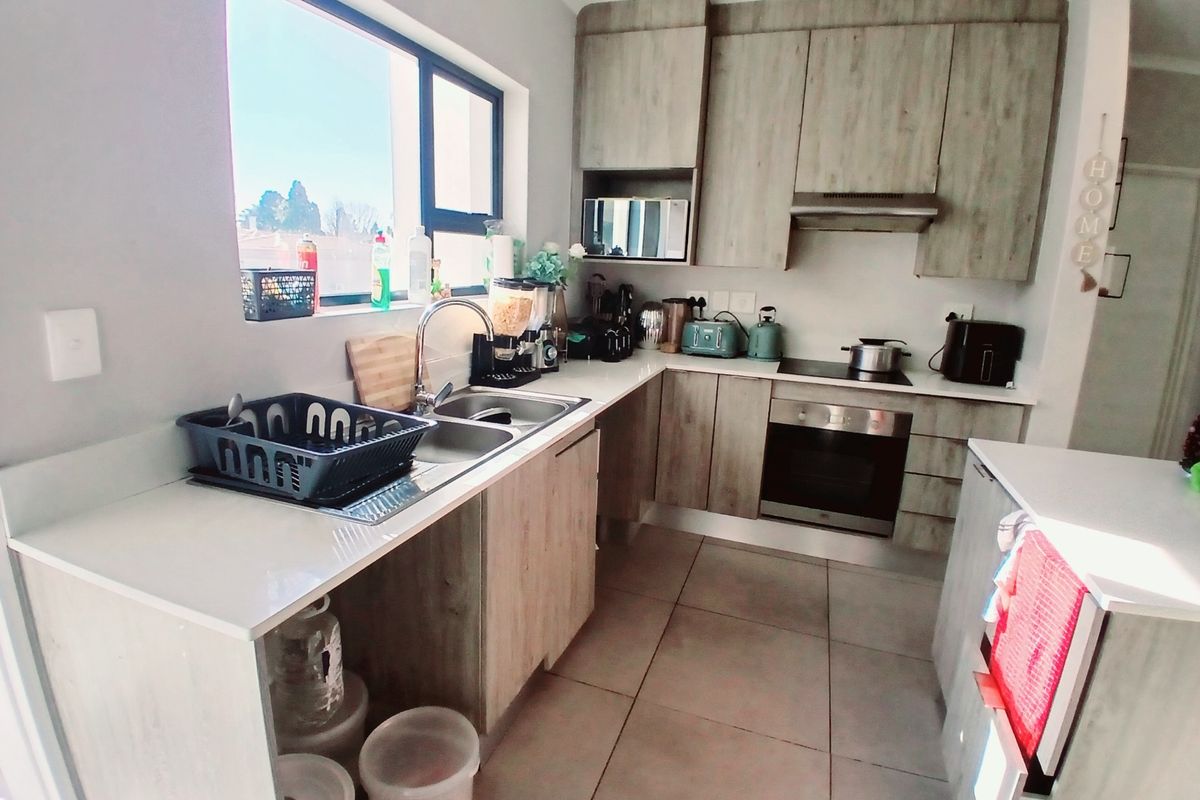 Modern kitchen featuring light wood-grain cabinetry, stone countertops, integrated oven, hob, and extractor fan with tiled flooring and ample natural light.
