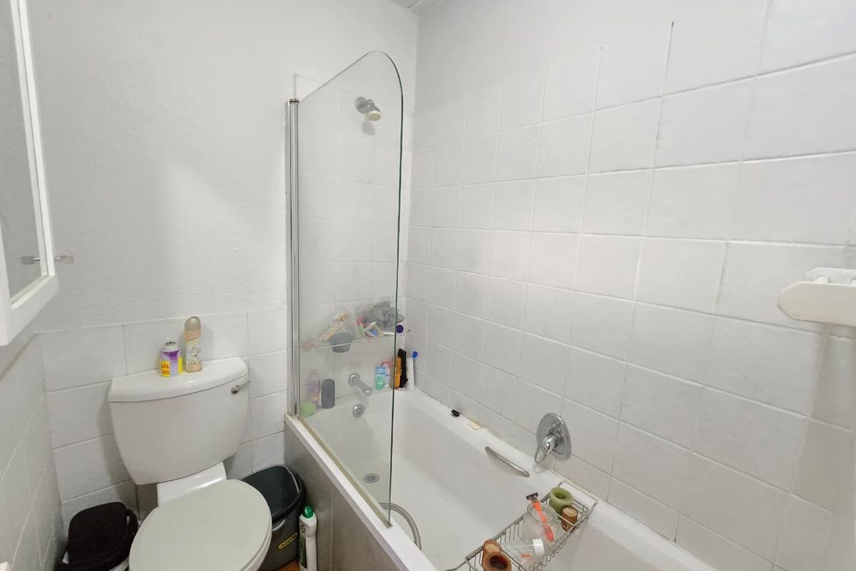 A functional bathroom featuring a white bathtub with a glass shower screen, wall-mounted shower head, and a standard toilet.