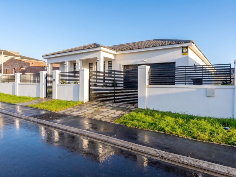 Modern single-story residence featuring a clean white facade, secure perimeter wall with horizontal slat fencing, paved driveway, and integrated garage.