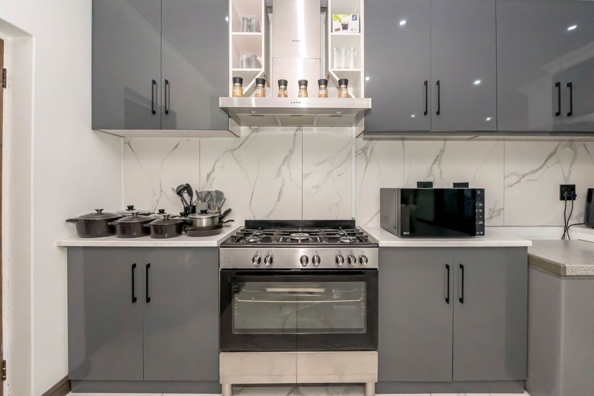 Modern kitchen featuring grey high-gloss cabinetry, a gas hob with stainless steel extractor, and elegant marble-look splashback tiles.