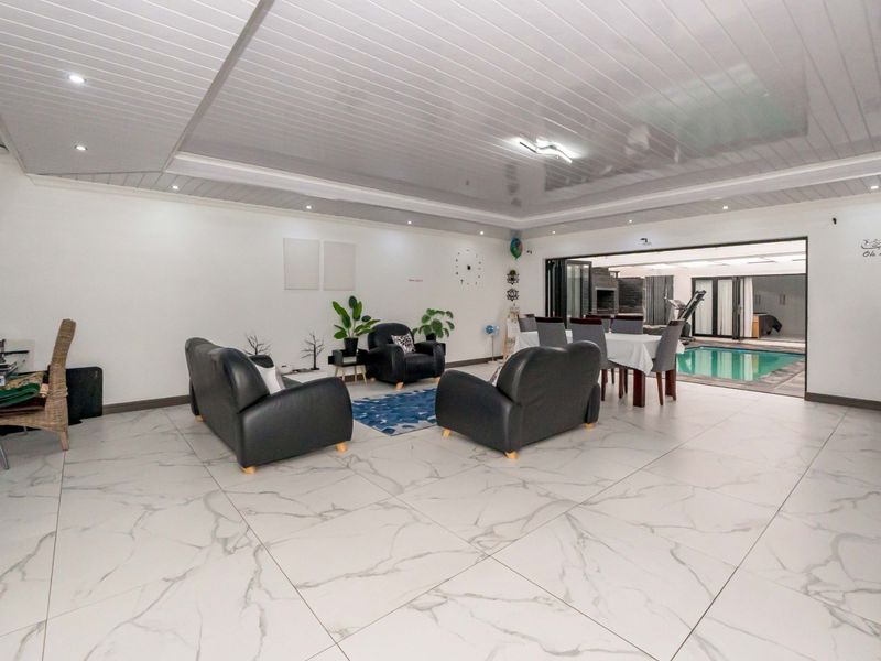 Spacious open-plan living and dining area featuring large marble-look floor tiles, recessed lighting, and seamless access to an indoor swimming pool via bi-fold doors.