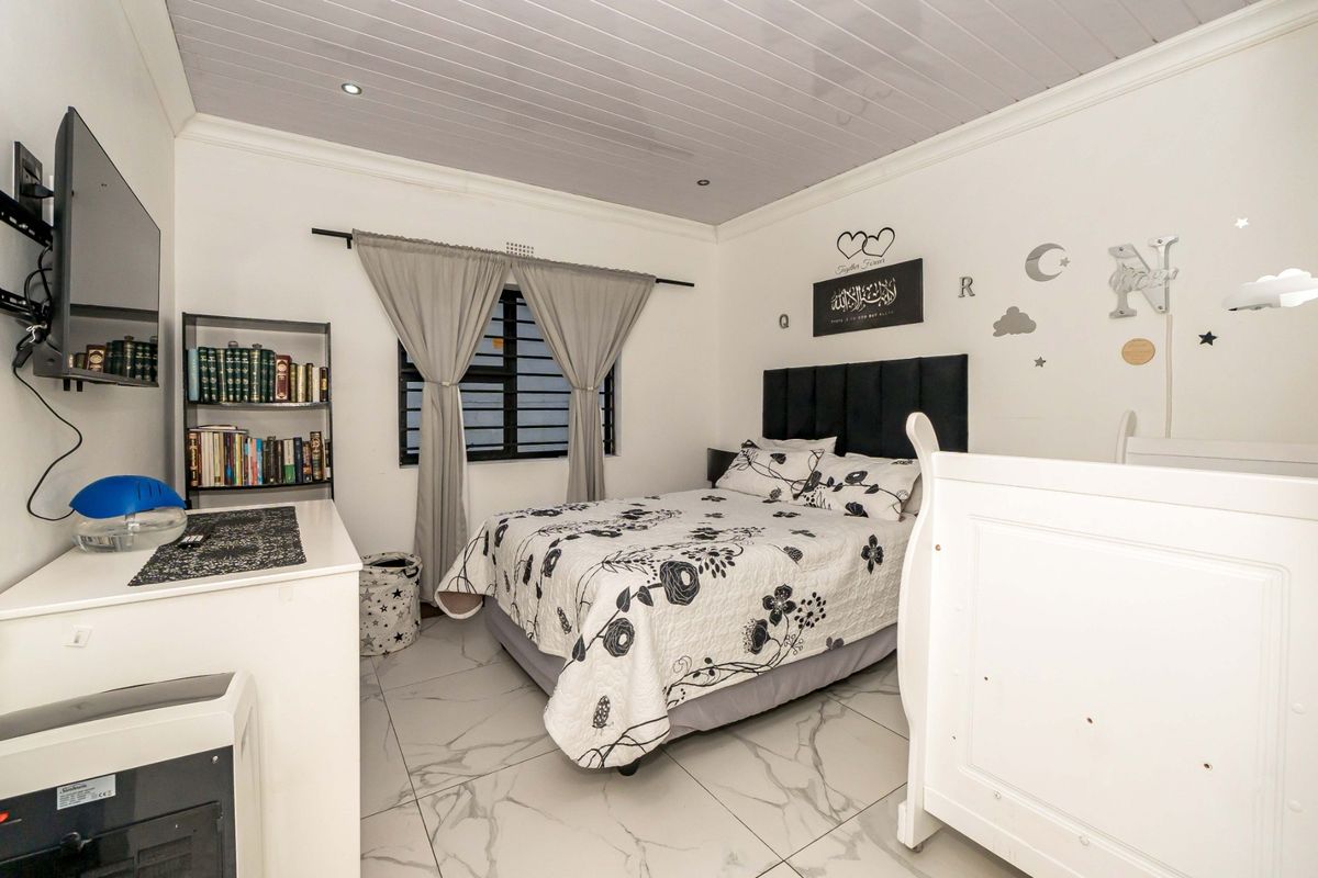 A well-maintained bedroom featuring modern marble-look floor tiles, a panelled ceiling with recessed lighting, and a window fitted with security bars.