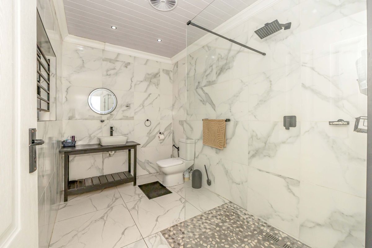 Modern bathroom featuring marble-look tiling, a spacious walk-in shower with a rain shower head, and a stylish vessel sink vanity.