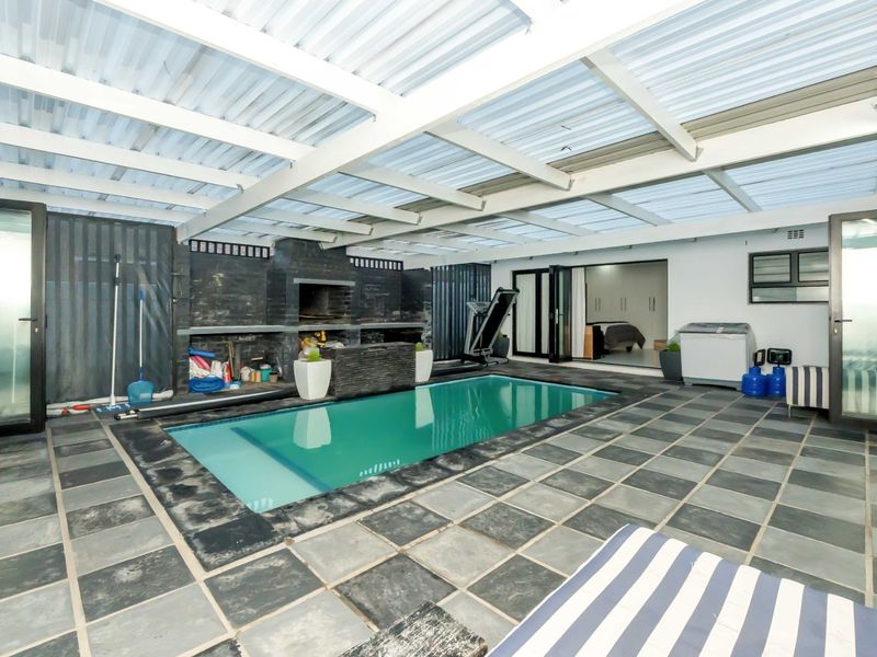 Covered pool area featuring a built-in braai, stone tile flooring, and direct access to the interior living space.