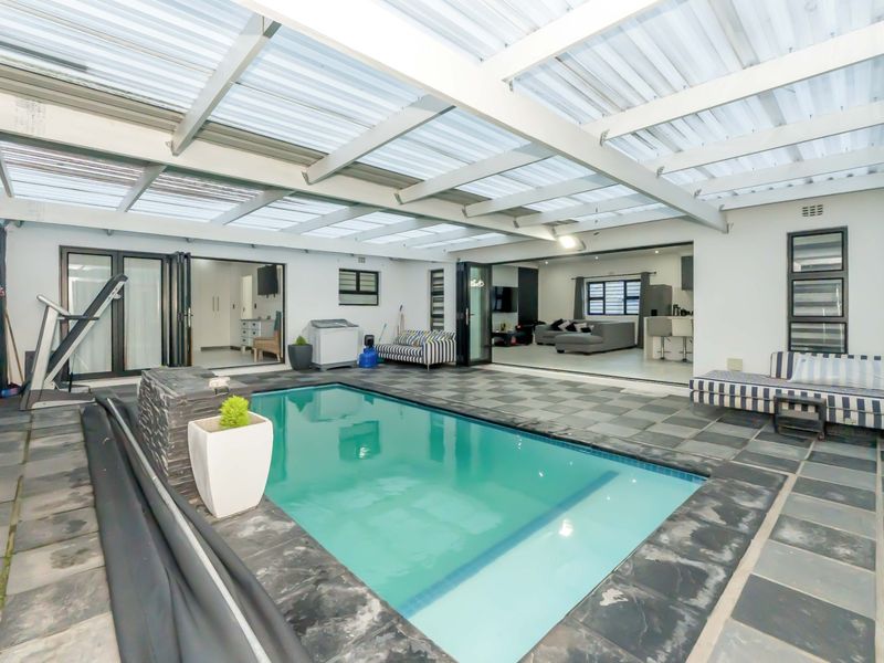 A covered outdoor pool area featuring stone tile flooring, a built-in water feature, and large stacking doors providing seamless access to the interior living space.