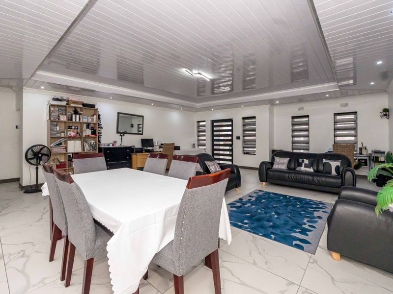 Spacious open-plan living and dining area featuring glossy ceiling panels, recessed lighting, and large marble-look floor tiles throughout.