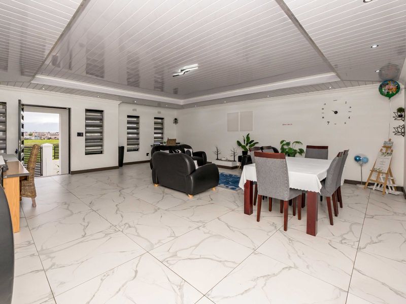 Spacious open-plan living and dining area featuring large-format marble-look floor tiles, modern glossy ceiling panels, and direct access to the outdoor area.